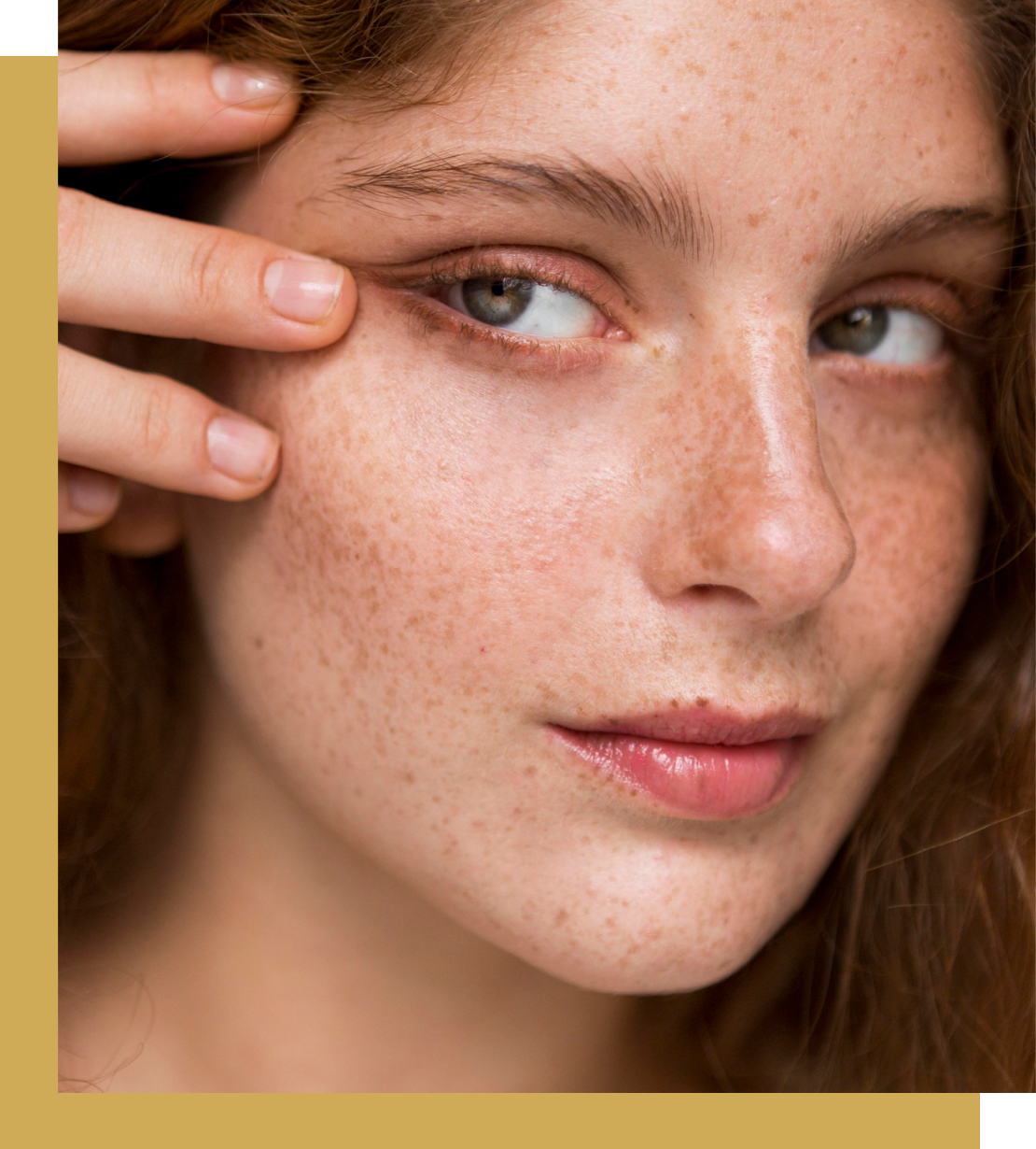 Close-up of a person with freckles touching their eye gently.